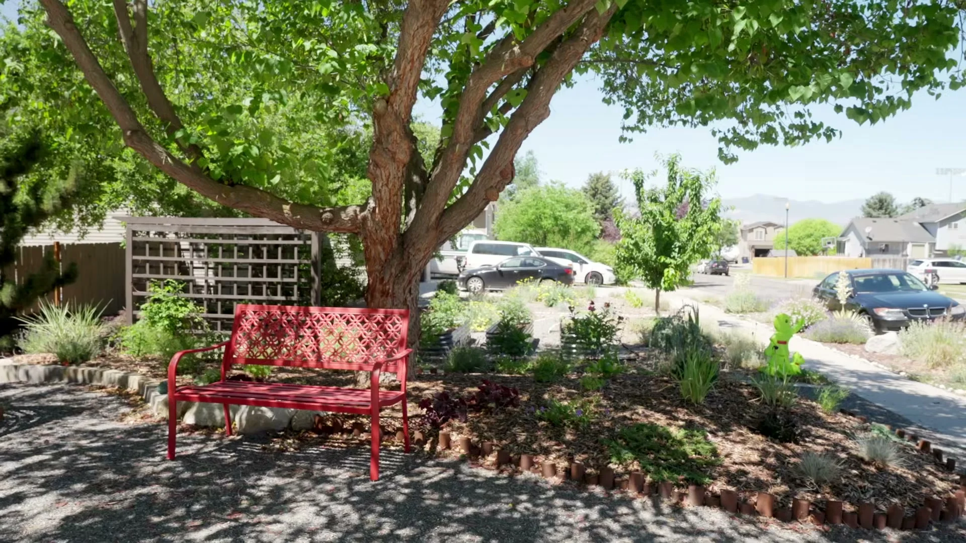 A red garden bench beneath a mature tree beside the planting beds and paths